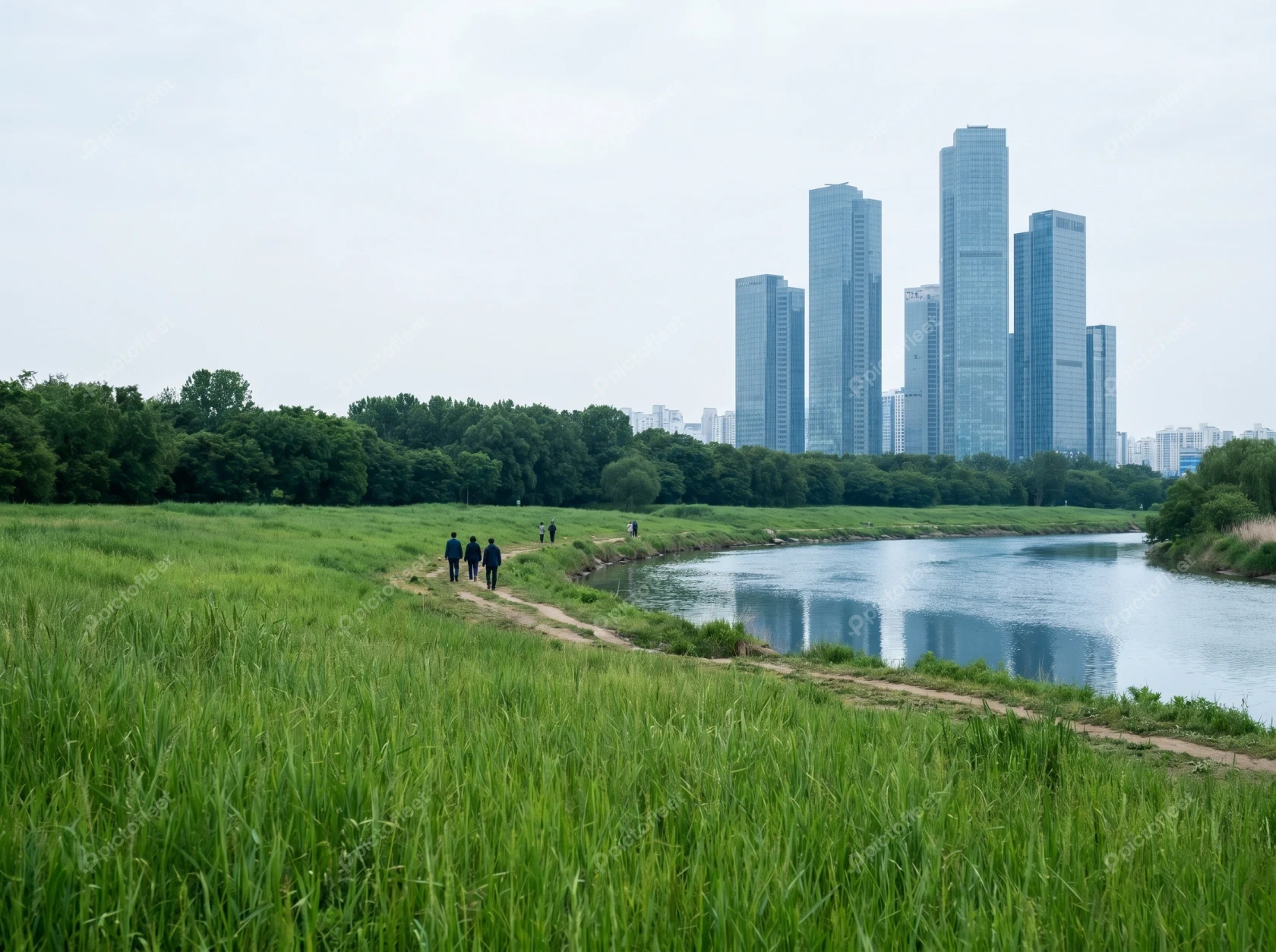 People walking along riverbank park with city skyscrapers background