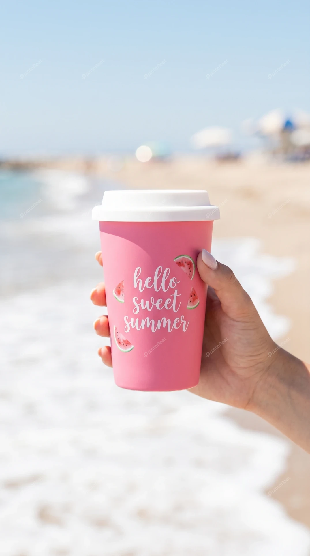 Hand holding pink hello sweet summer cup at the beach
